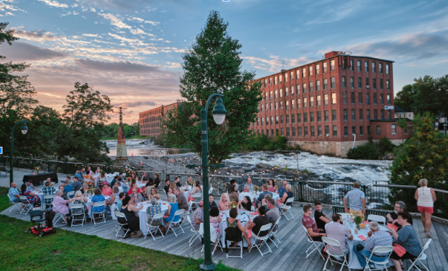Picture of people sitting at tables with dam in the background at Feast of the Falls